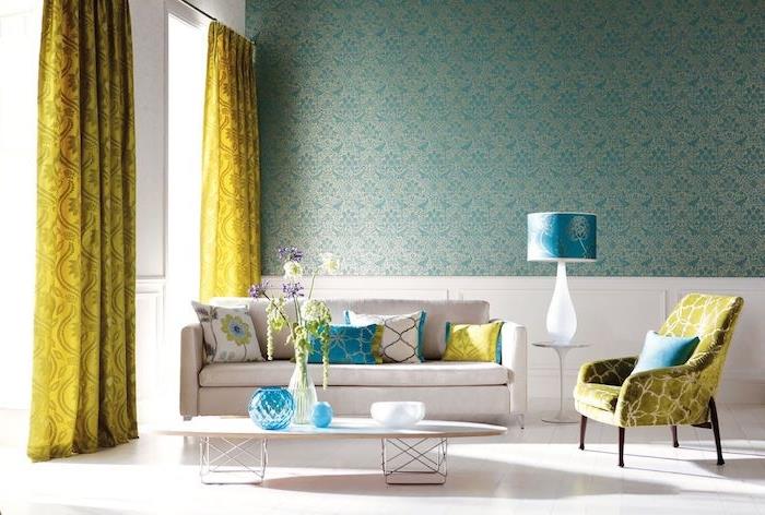 naftos mėlynos spalvos tapetai ant sienos, balta sofa ir žurnalinis staliukas, baltos grindys, barokinės geltonos užuolaidos, nedideli turkio spalvos atspalviai