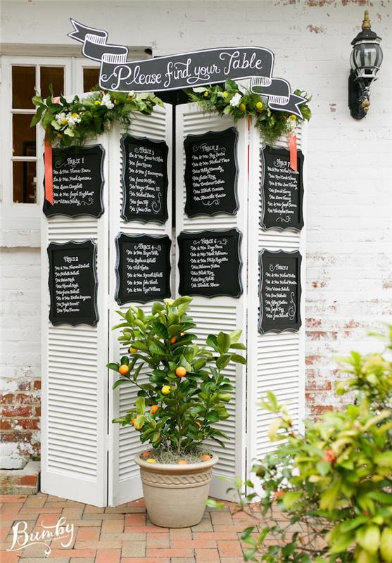 baltas ekranas su lentomis, svečių vardai parašyti balta, žalia girlianda, apelsinų medžiu, vestuvės lauke