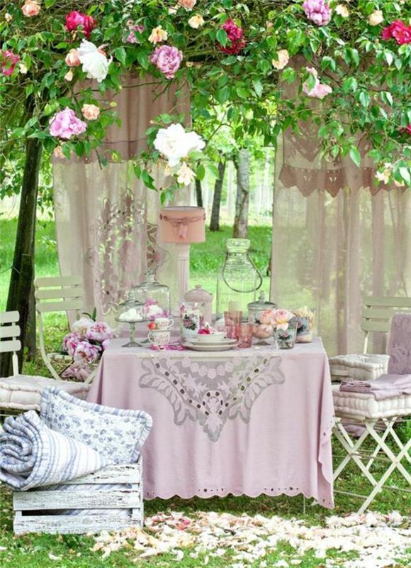 Beyaz katlanır sandalyeler üzerinde leylak masa örtüsü ve leylak minderli bahçe masası ile bahçe tasarımı örneği çiçeklik fikri