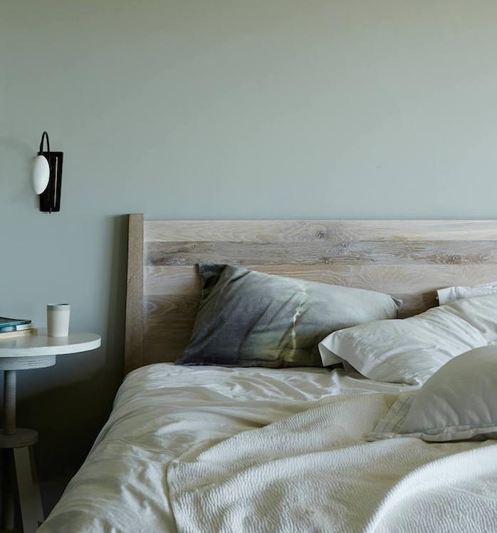 sivo zelena ideja stenskega slikanja, lesena postelja, belo posteljnina, sive, rumene blazine in beljena lesena miza