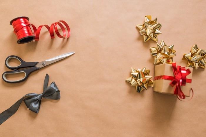 Kalėdiniai tapetai, „pasidaryk pats“ dovanų pakavimo projektas iš amatų popieriaus, auksinės popieriaus žvaigždės, raudona dekoratyvinė juostelė, juodi lankai ir žirklės