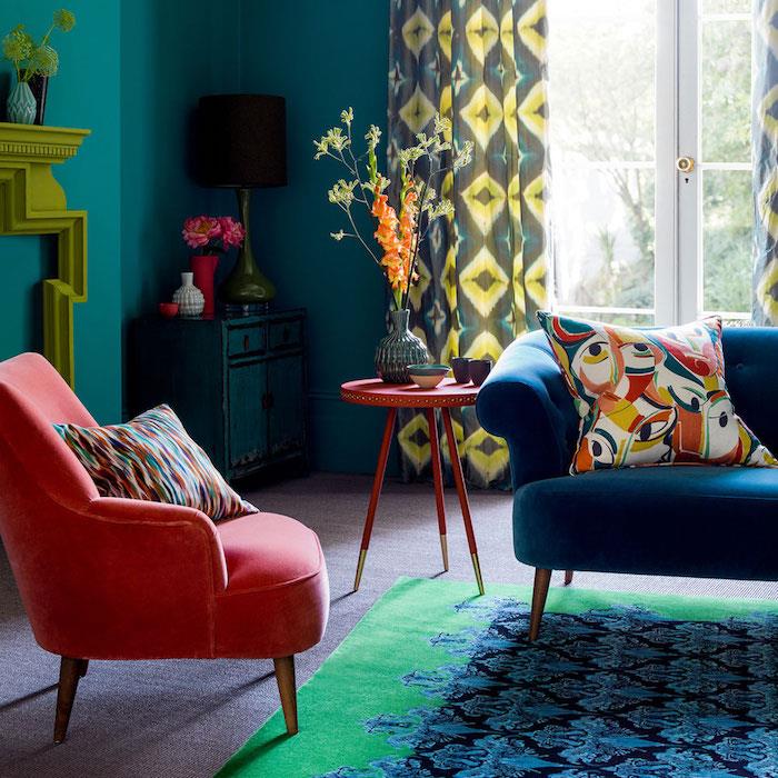 modra t rdeča dekoracija dnevne sobe z račjo modro barvo, modrim kavčem in modro -zeleno preprogo, rdečim naslanjačem, dizajnerskim kaminom, barvnimi zavesami in okrasnimi blazinami
