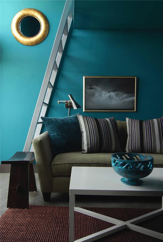 anties mėlynos svetainės dekoras kaip sienų tapybos pasirinkimas, apvalus veidrodis, alyvuogių žalia sofa, antis, pilkos, juodos ir baltos pagalvėlės, raudonas rudas kilimas, baltas kavos staliukas