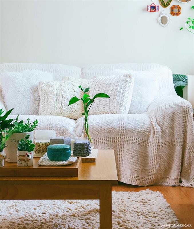 čakalna dnevna soba, bela krznena preproga, lesena mizica, kavč z belo pleteno odejo, pletena prevleka za blazino, zelene rastline