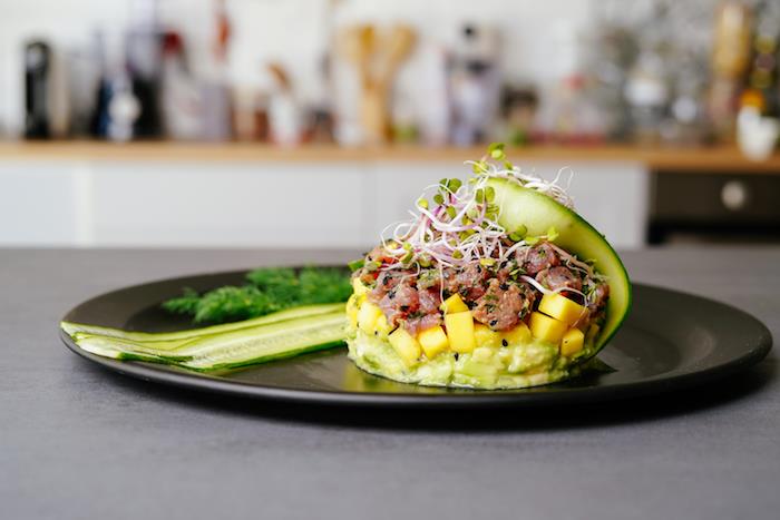 avokado ir lašišos tartaro su mango sluoksniu, juodųjų sezamų sėklomis ir agurkų bei daigų puošmena