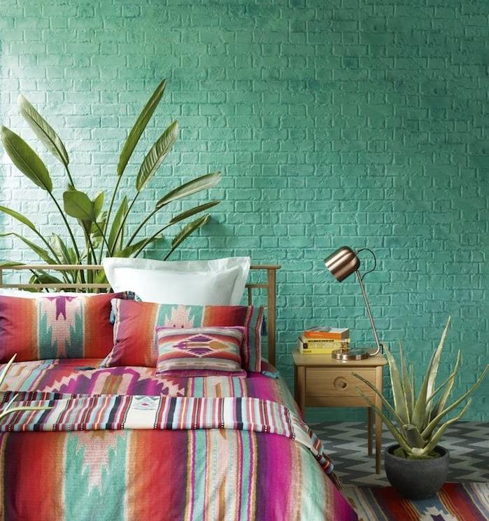 barva spalnice za odrasle, opečnata stena prebarvana v zeleno, boemsko elegantno posteljnina z barvitimi vzorci, sivo -bela talna obloga, oblikovalska svetilka, zelene rastline