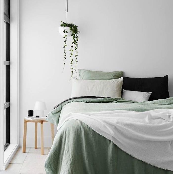 dekoracija spalnice za odrasle, bela stena, belo in zeleno posteljnina, črna blazina, lahek parket, lesena nočna omarica, viseča zelena rastlina