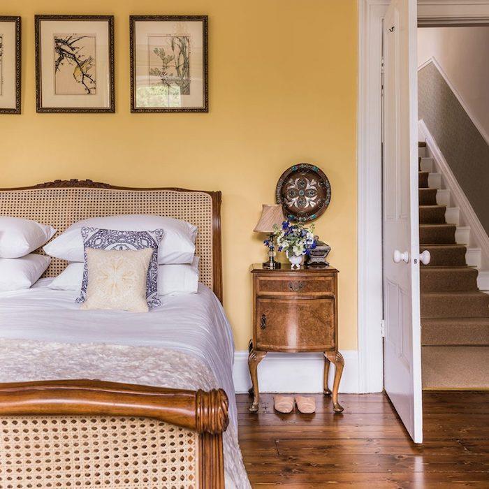 dekoracija spalnice za odrasle, rumena stena, vintage lesena postelja, rjav parket v retro elegantnem podeželskem slogu