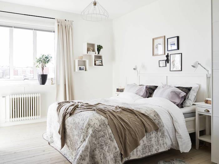 Ideja za dekoriranje spalnice v zapečkanju, parket iz svetlega lesa, rjava, siva in bela posteljnina, temno modre blazine, bela stena