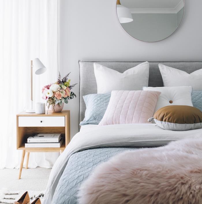 dekoracija spalnice, bela, roza in pastelno modra posteljnina, lesena nočna omarica, šopek rož, svetlo siva preproga