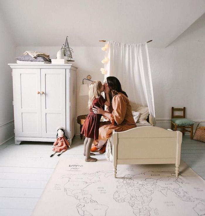 vaikų miegamasis po šlaitu baltas su žemai balta lova, žema spintelė, maža kėdė, pasaulio žemėlapio kilimas ant balto skandinaviško parketo