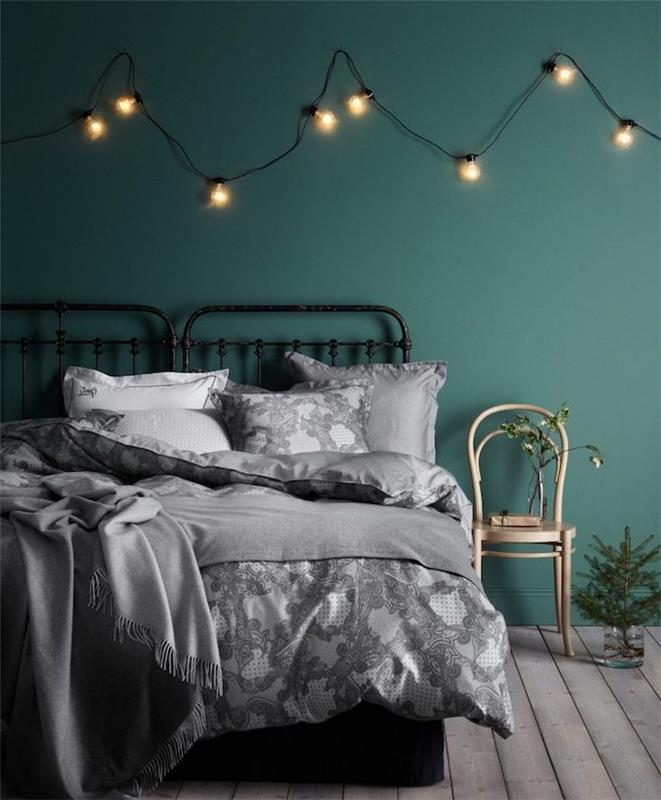 dekor glavne spalnice s temno zeleno barvo za stene in svetlim dekorjem, lesena tla, belo in sivo posteljnina na črni kovinski postelji