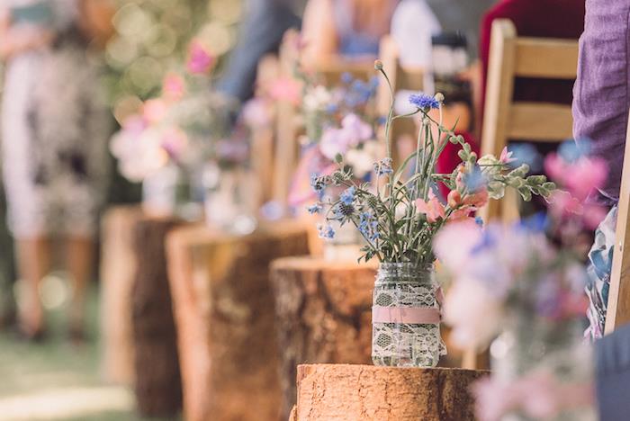 okrasitev podeželske poročne slovesnosti v lesenih hlodih, okrašenih s steklenimi kozarci, okrašenimi s čipkami in rožnatim trakom ter rožami
