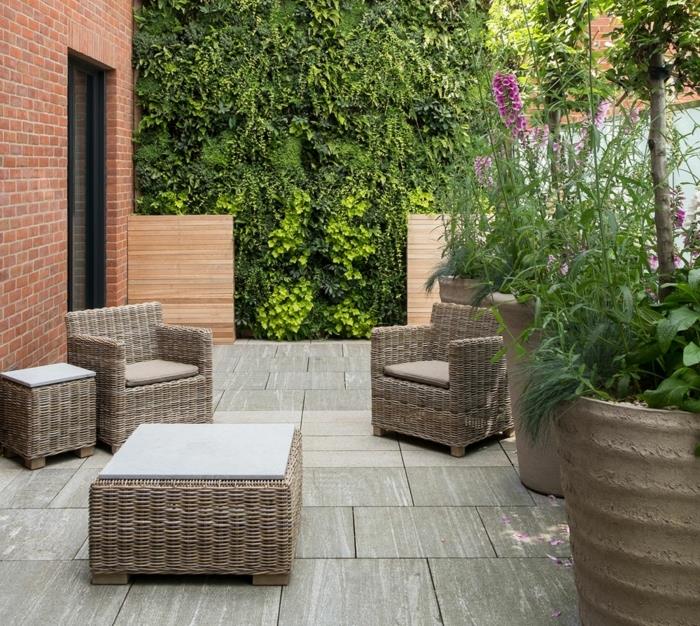 geniali sodo idėja, kiemo sodo baldai akmens plokštėse, rotango foteliai ir stalai, žalia siena ir dideli gėlių vazonai