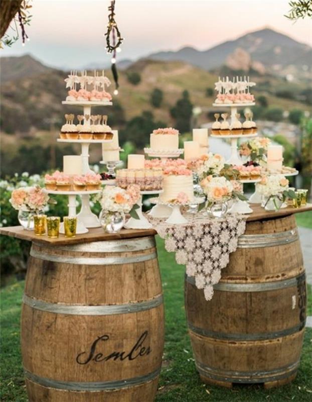 rustik düğün dekorasyonu, ahşap fıçılar ve masa olarak ahşap tahta, küçük kekler, kekler, pasta teşhiri, çiçek desenli masa örtüsü, kokteyller, çiçek dekorasyonu, dağ manzarası
