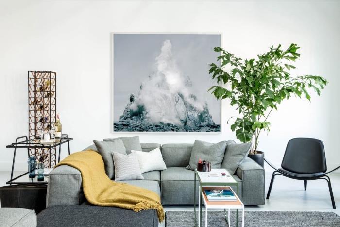 gri kanepe ve halı, hardal sarısı battaniye, beyaz zemin ve duvar kaplaması, yeşil bitki, duvarda dekoratif çerçeve boyama