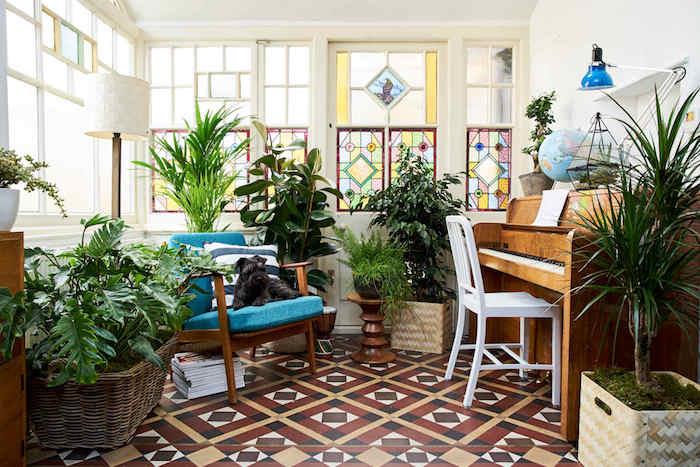 orientalska dnevna soba s ploščicami, piango in leseni naslanjač z modro blazino, ideja sobne rastline v loncu na tleh in na mizi, barvna vitraža