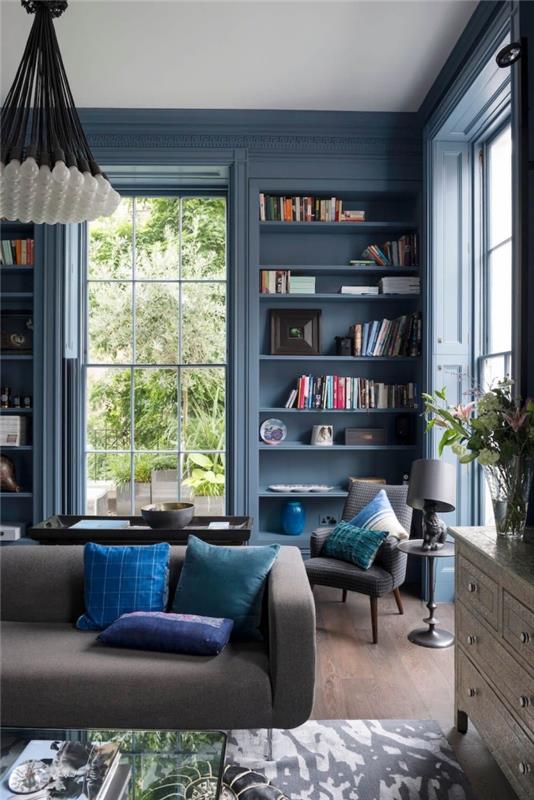 alanı yapılandırmak ve derinlik vermek için lacivert boyalı kitaplık duvar ve çerçeve ile mavi ve gri oturma odası