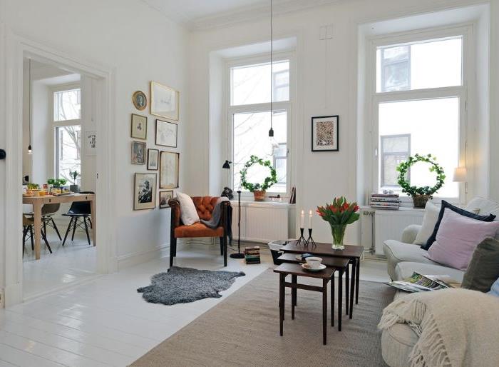 Jauki balta svetainės dekoro idėja su patogia perlamutrine pilka sofa, balintos parketo grindys, mediniai stalai, baltos sienos, dekoruotos rėmeliais