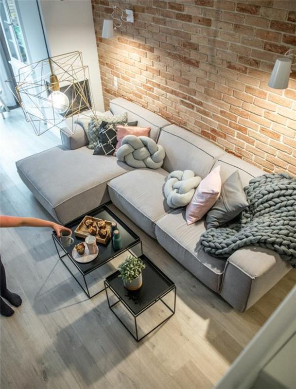 svetainės dekoras, perlų pilka kampinė sofa, pilka megzta pledas, juodi lizdai,