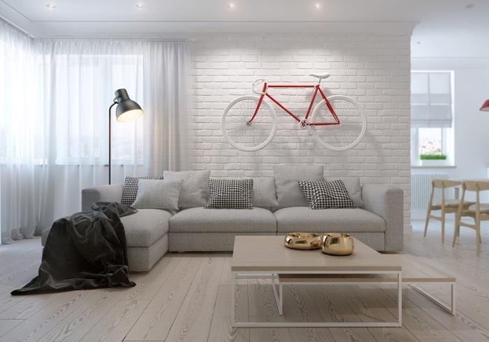 Oturma odasında İskandinav mobilyaları, gri kanepe, hafif parke, ahşap ve metal zigon sehpalar, hafif parke, beyaz tuğla duvar, kırmızı ve beyaz bisiklet duvar dekorasyonu