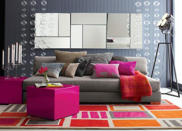 svetainės dekoro idėja, rožinės ir oranžinės spalvos kilimas, violetinės išmatos, pilka siena, senoviniai žvakidės