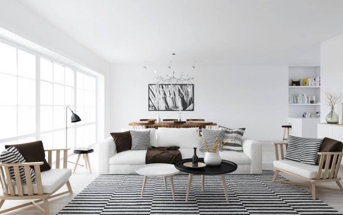 İskandinav evinde modern oturma odası, siyah beyaz halı, beyaz kanepe, beyaz koltuk minderli ahşap koltuklar, siyah beyaz ve kahverengi dekoratif minderler, ahşap sandalyeler ve masa ve grafik boyama duvar dekorasyonu