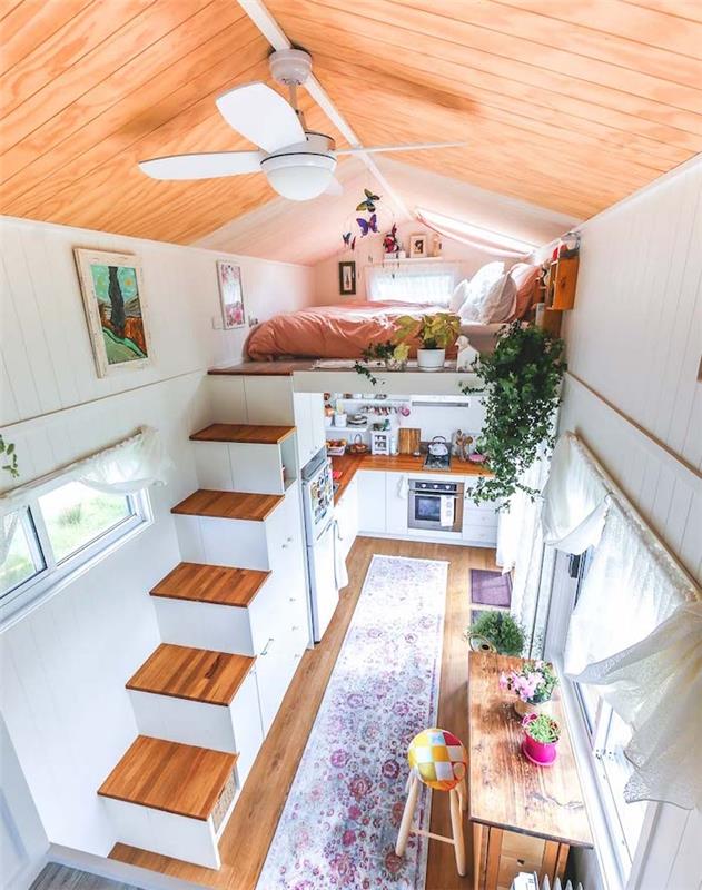 ideja o dekoriranju majhne hiše, garsonjera s posteljo na podstrešju, leseno stopnišče, bela in lesena kuhinja v medetaži, poudarki urbane džungle