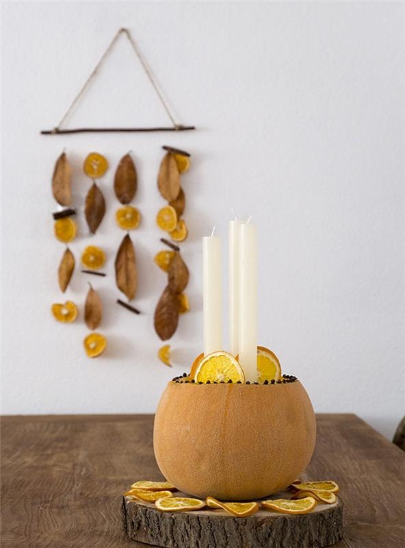 stenski dekor iz visečega lesa s suhimi rezinami pomaranče in jesenskimi listi, sredino buč s svečami na lesenem hlodu in pomarančnimi rezinami