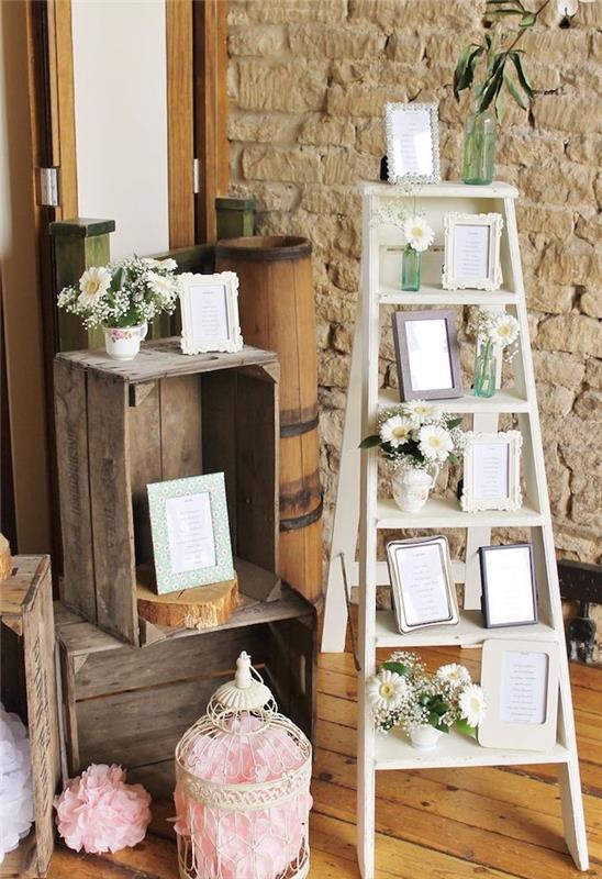 vestuvių stalo planas su baltomis kopėčiomis ir senoviniais nuotraukų rėmeliais, gėlių vazos su mažomis gėlių puokštėmis, medinės dėžės, apleistas prašmatnus paukščių narvas, vestuvių stalo planas vestuvių dekoravimas