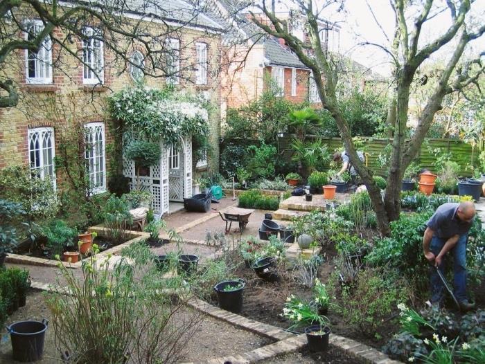 kraštovaizdžio dizainas, angliškas kotedžo stiliaus namas, sodas su keliomis skirtingo aukščio sodintomis aikštėmis, įėjimas gėlių arkoje, medžiai ir gėlės