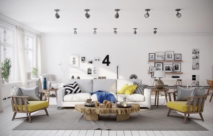 İskandinav oturma odası dekoru, gri halı, kirli beyaz kanepe, sarı koltuk minderli ahşap sandalyeler, rustik ahşap masa, siyah beyaz çizimler ve fotoğrafların duvar dekorasyonu