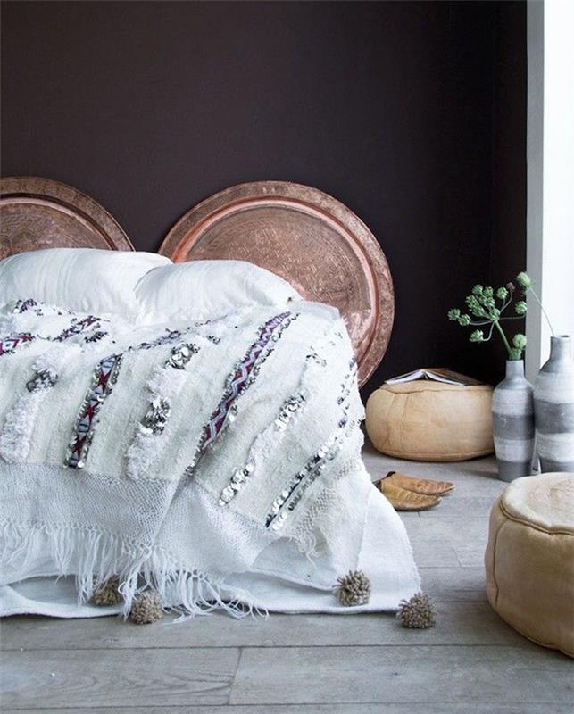 umazano belo posteljnina, črna stena, okrašena z lesenimi hlodi, siv parket, bež otomanke, bela in siva vaza, orientalska dekoracija spalnice