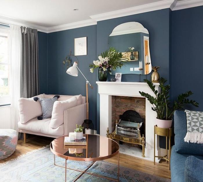 okrasni kamin v dnevni sobi z modrimi stenami z ogledalom, svetlo roza naslanjač, ​​bakrena mizica, okrasne rastline