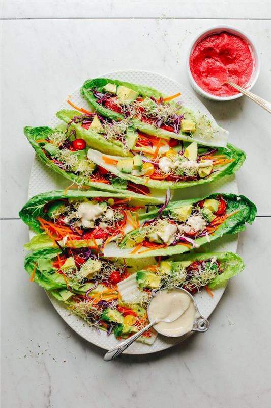 vegetarijanski recept za tacos iz listov solate, okrašen z avokadom, češnjevimi paradižniki, kalčki lucerne in humusovo omako