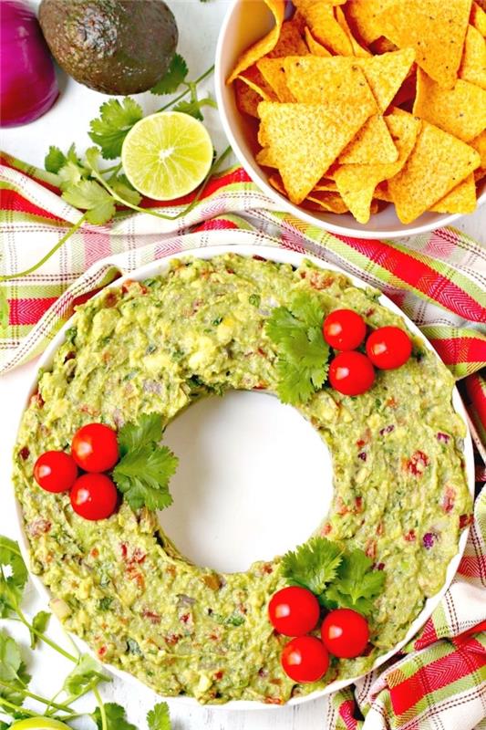 Tortilla cipsi, orijinal Noel aperitifi, ev yapımı sos ile servis yapmak için kiraz domates ve maydanozla süslenmiş Meksika guacamole ile Noel çelengi