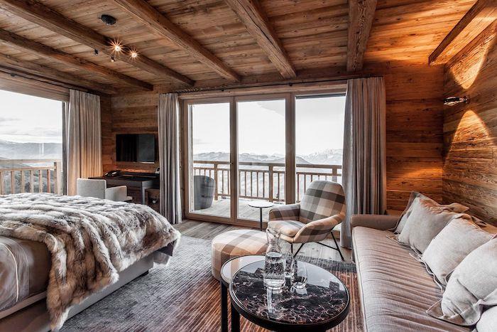 Notranjost brunarice, udobna lesena koča, udobna postelja in sedežna garnitura s kavčem, veliko okno s čudovitim razgledom, balkon s pogledom na gore