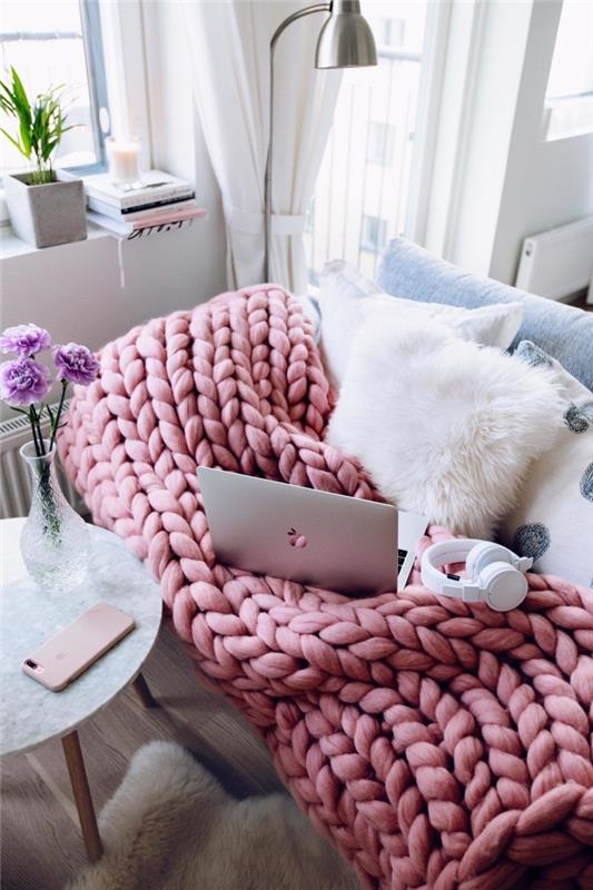 sofa paversta mažu jaukiu kampeliu su kokoniška pagalve baltu kailiu ir dideliu saldainiu rožiniu tinkleliu
