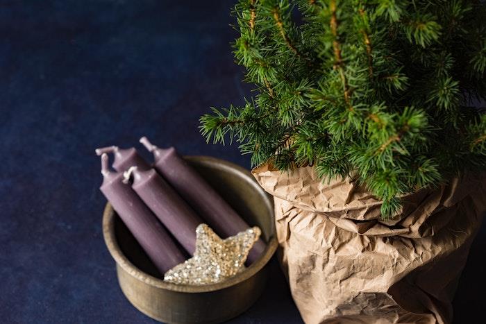 Kalėdiniai tapetai iš žalių pušų šakų kraftpopieriniame maišelyje, violetinės žvakės ir auksinė žvaigždė pilkame dubenyje