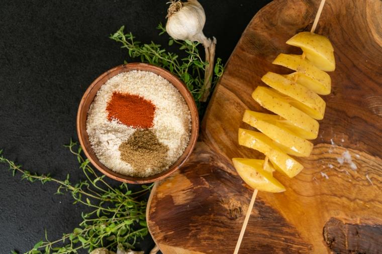 Imburrare hasselback krompir, ciotola di legno con parmigiano grattugiato e spezie