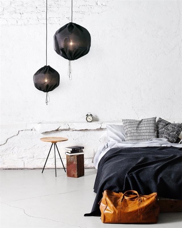 Yatak odasında İskandinav tarzı dekor, soluk beyaz duvar, siyah sarkıt lambalar, gri, beyaz ve siyah nevresimler, ahşap ve metal komodin