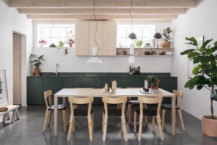 İskandinav mobilyaları, masif ahşap masa, ahşap ve siyah deri sandalyeler, koyu yeşil mutfak önü ve açık kirişler, yeşil bitki dekorasyonu