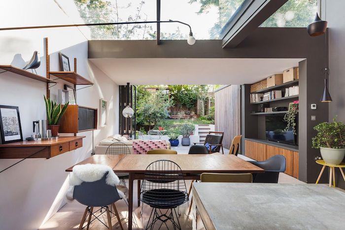 moderni virtuvė, atsiverianti į modernią svetainę, uždengtą po pratęsimo stogu su balta sofa, medine televizoriaus spintele ir kėdėmis