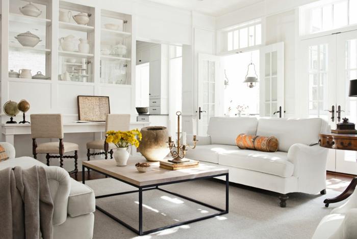 elegantna podeželska dnevna soba, beli kavč, biserno sivi stoli. lesena in kovinska miza, bela porcelanska omara, bela škatla, okrasna vaza