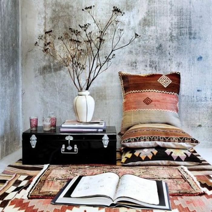 etninis audinys, pagalvėlės su geometriniais raštais, pilkas tinkas, vaza su sausomis gėlėmis
