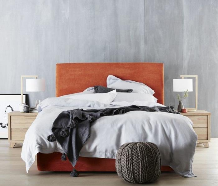 bledo siva posteljnina, pleteni puf, oranžni posteljni okvir, siva stena, lesene nočne omarice, deko