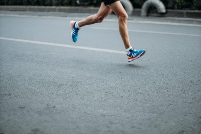 kojos su mėlynais sportbačiais ir vyras, bėgantis gatve