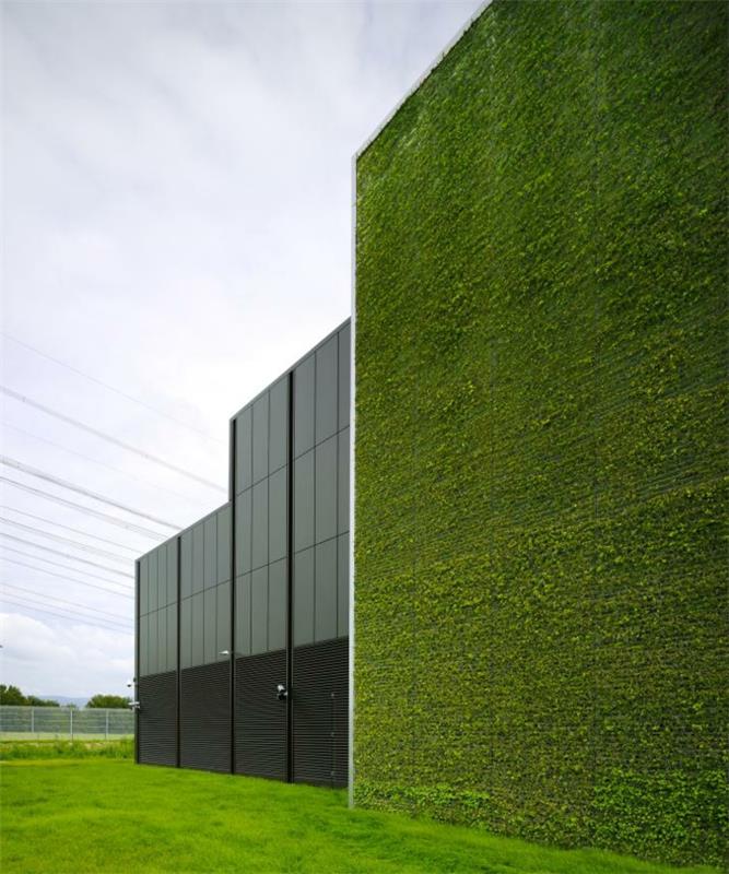 pramoninis pastatas su išorine žalia siena, dalis pastato yra juodo metalo ir juodų langų, didelis žalias laukas
