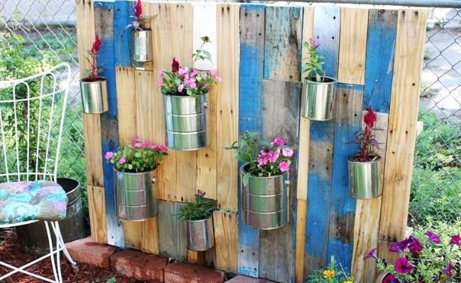 lauko augalinė siena iš medinių padėklų, ant jos kabančios metalinės dėžutės, rožiniai gėlių augalai, pasidaryk pats sodo dekoras