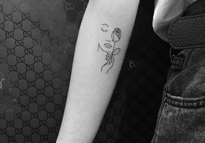 minimalistična tetovaža v ženskem dizajnu z risbo na roki v preprostih črtah, ki prikazujejo ženski obraz in majhno roko z vrtnico